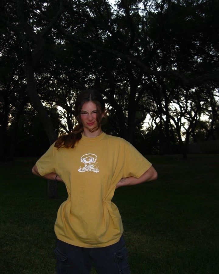 Person wearing a yellow t-shirt with a logo in a dark outdoor setting