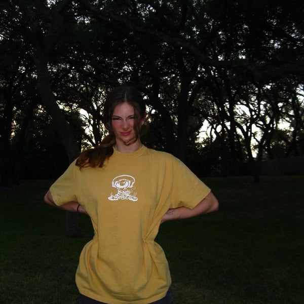 Person wearing a yellow t-shirt with a logo in a dark outdoor setting