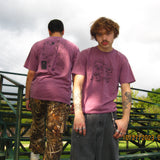 Two people wearing matching purple t-shirts outdoors with a green metal structure in the background.
