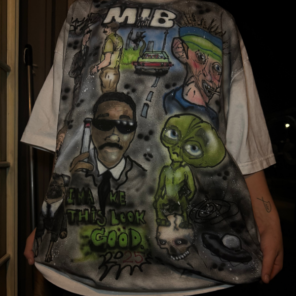 T-shirt with graphic design featuring characters and text, held by a person.
