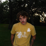 Person wearing a yellow t-shirt with a graphic design, standing outdoors with trees in the background