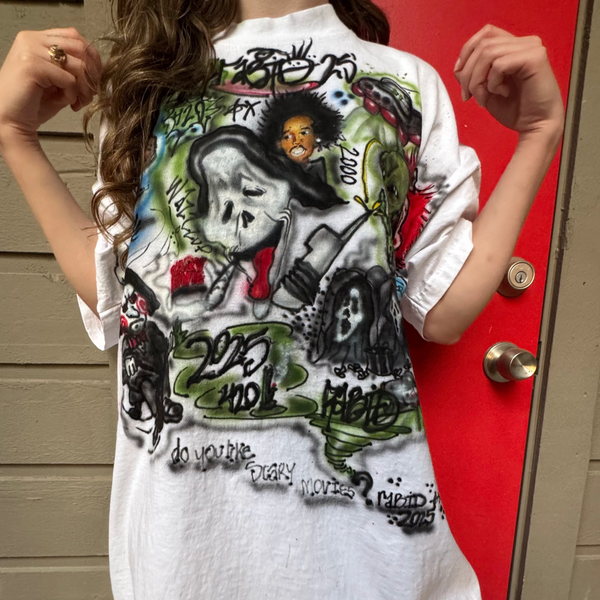 Person wearing a white t-shirt with graphic designs in front of a red door.