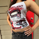 Person wearing a white tank top with colorful graphics and text, standing in front of a red door.