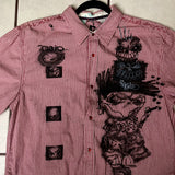 Red checkered shirt with black graphic designs on a hanger against a tiled wall.