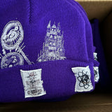 Purple beanie with white embroidered designs on a cardboard surface