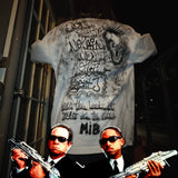 Two men in suits holding guns in front of a graffiti-covered wall.